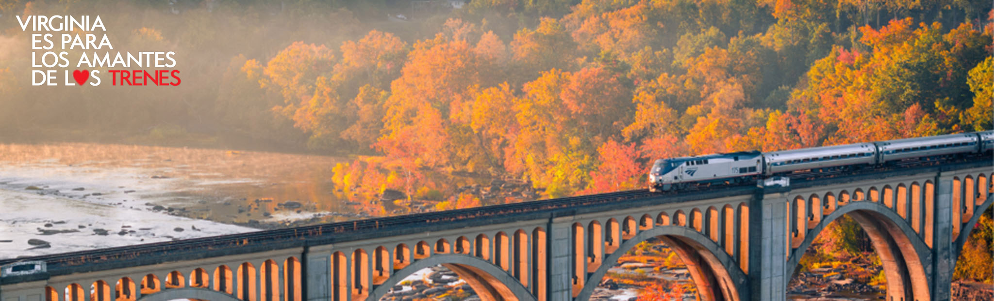 Un tren de Amtrak cruza un puente al atardecer, con un logotipo de "Virginia is for Rail Lovers" en una esquina